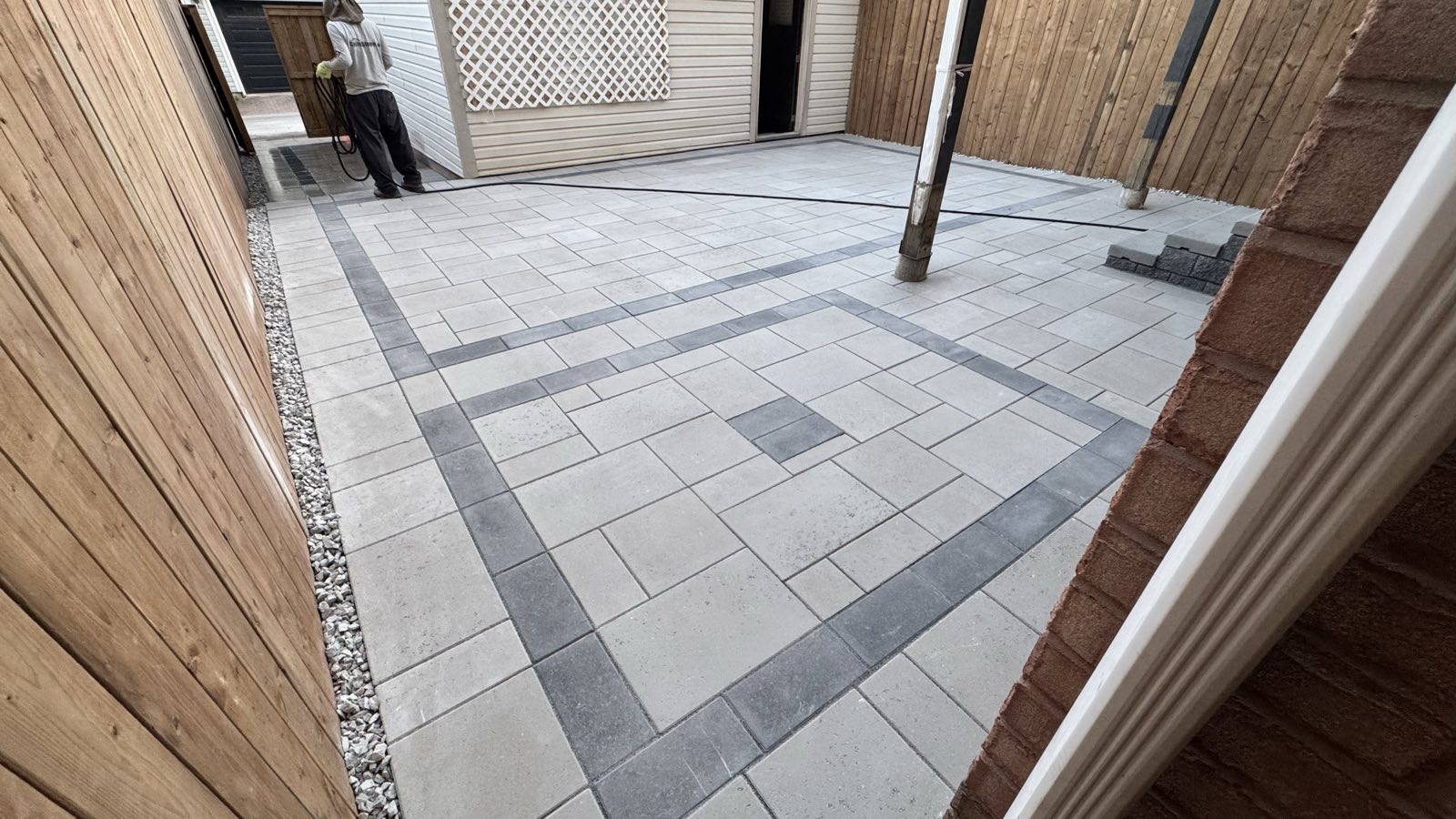 Large-format grey paver patio in an Oakville backyard with charcoal banding and gravel drainage strips along a cedar fence